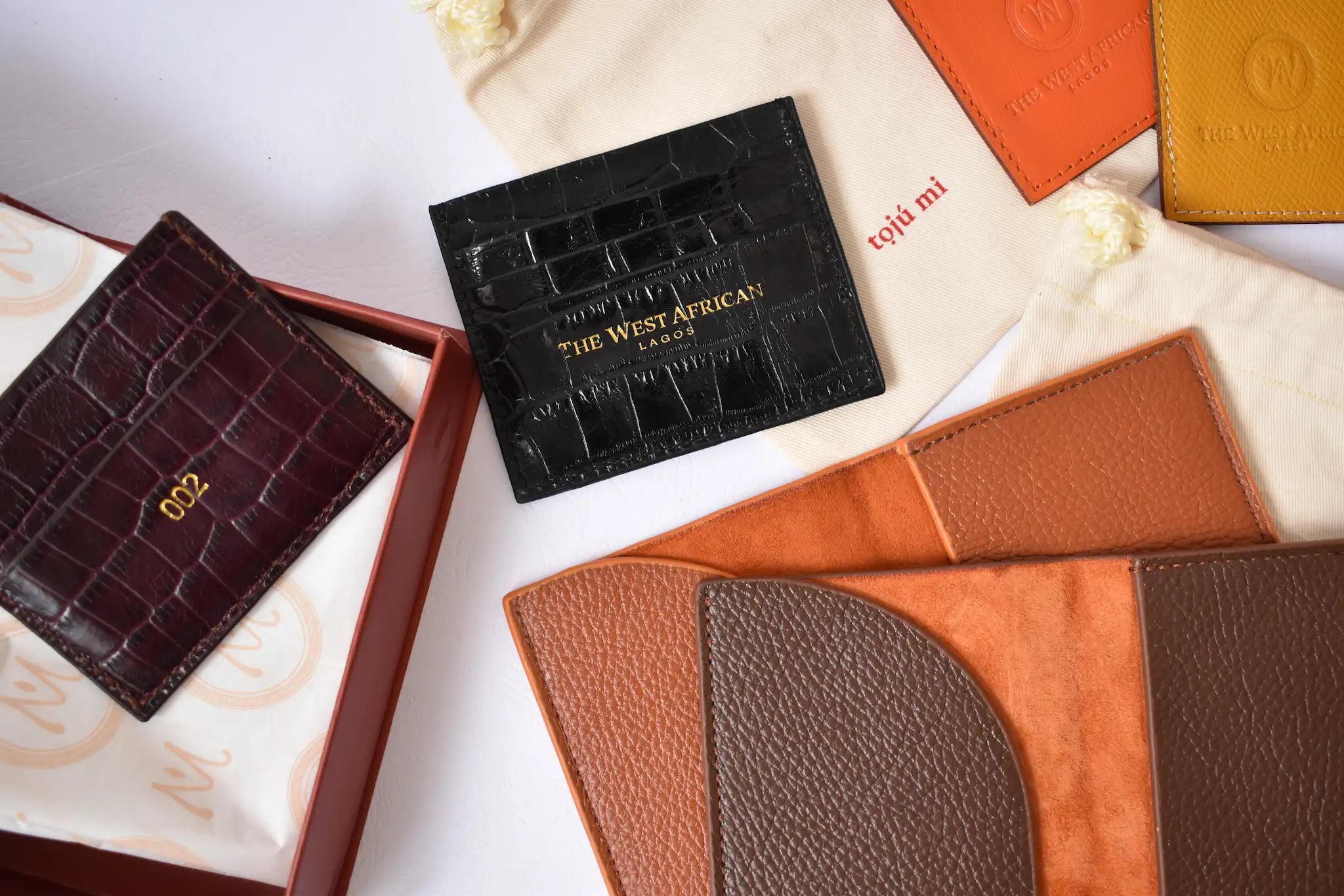 Collection of leather wallets and boxes with 'The West African' branding on a white surface.